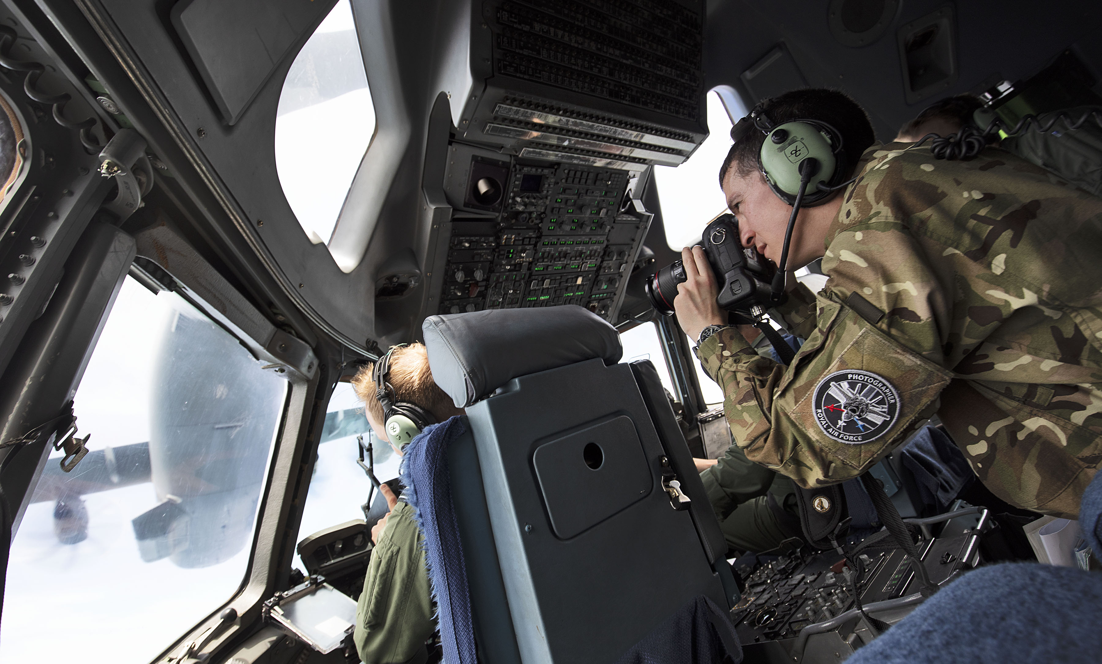 Pilots in the cockpit with camera equipment, looking out to another aircraft in flight.